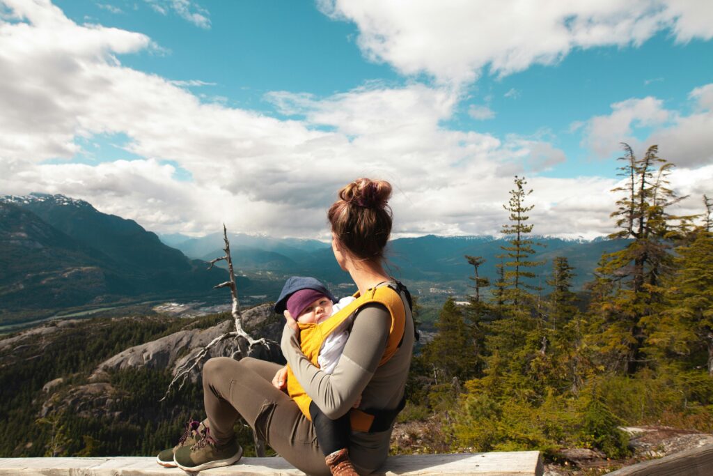 A mother sits with her baby overlooking a scenic mountain landscape, enjoying nature's beauty.